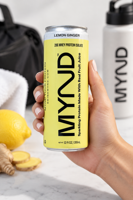 Hand holding a yellow can of MYND Lemon Ginger sparkling protein water with 20g whey protein isolate.